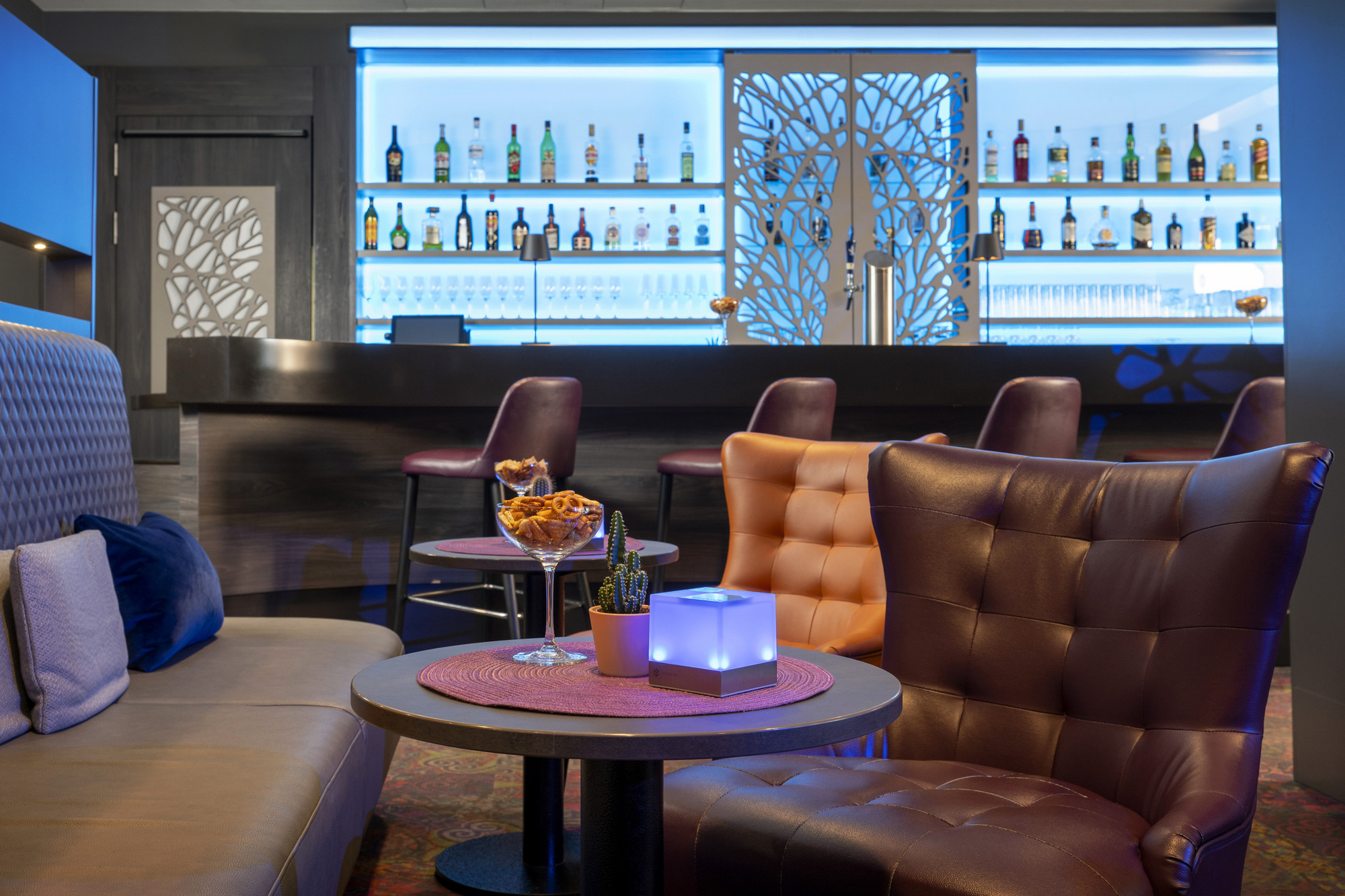 Gemütliche Lounge mit Sitzgruppen, Sofas, Sesseln, stimmungsvollen Lichtern und Kamin vor der Hotelbar 