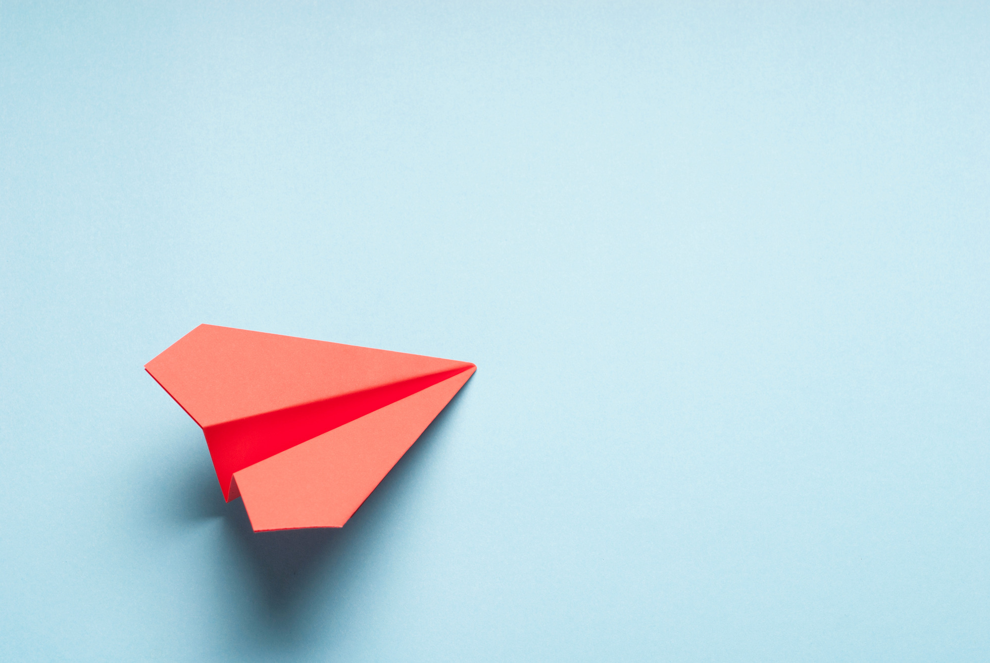 Symbolbild mit rotem Papierflieger vor einem blauem Hintergrund